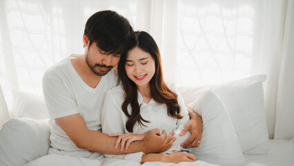 Pregnant Asian couple relaxing together in bed, showing love and care