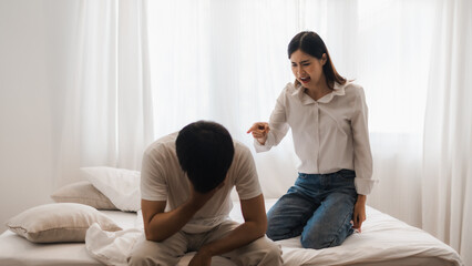 Young woman arguing with her boyfriend sitting on bed at home, blaming him for problems