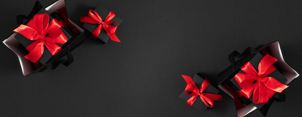 Top view panoramic photo of black gifts with red satin ribbons and bows on isolated black...
