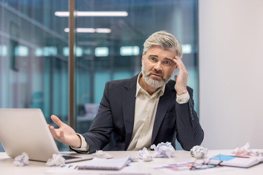 Stressed businessman sitting at desk in office with papers and laptop