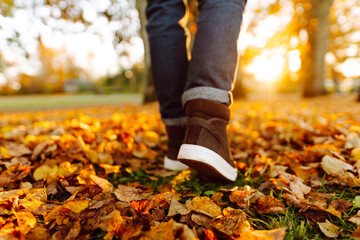 A close-up of a man in boots walking along a path strewn with bright autumn leaves. A man in shoes walks in an autumn park on a sunny day. The concept of seasonality, walks.