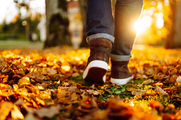A close-up of a man in boots walking along a path strewn with bright autumn leaves. A man in shoes...