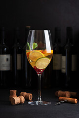 Sangria with citrus fruits and mint, corks and a corkscrew on a dark table with wine bottles.