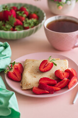 Crepes with chocolate spread and fresh strawberries, served with tea on pink background