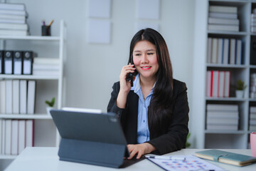 Asian businesswoman talking on phone and working on tablet in office