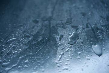 Close-up of clear water droplets on a cold, smooth surface. The abstract texture with a blue tint is ideal for backgrounds related to weather, cleanliness, or moisture.
