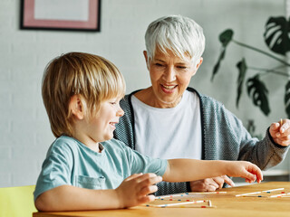Portrait of grandmother and grandson having fun together playing board game pick-up sticks at home