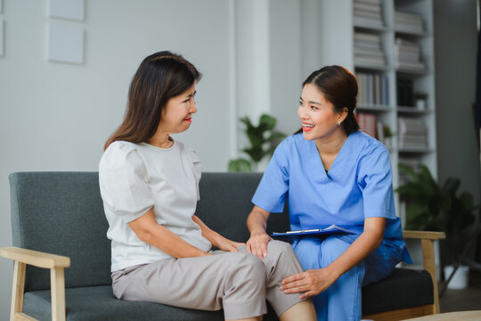 Asian nurse examining knee of female patient during home visit