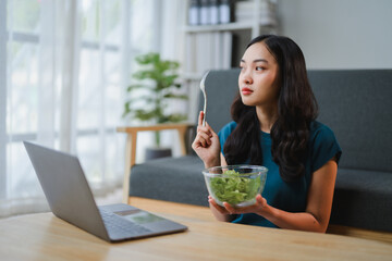 Young woman eating salad while working from home
