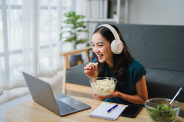 Young Woman Watching a Movie on Laptop and Eating Popcorn at Home
