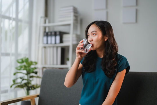 Young asian woman drinking fresh water from glass in office