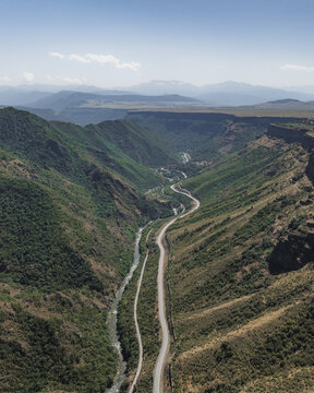 Aerial view of a serpentine road carving through a verdant canyon, a ribbon of grey against the lush greens, under a vast blue sky, Lori, Lori Province, Armenia.