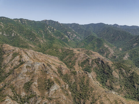 Aerial view of rugged, sun-baked mountains with sparse vegetation contrast sharply against the verdant, dense forests clinging to the slopes, Lori, Lori Province, Armenia.