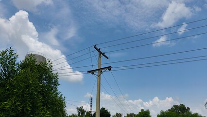 Electric power lines on a pole with a cloudy blue sky in the background