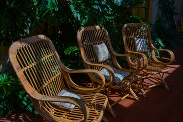 Three wicker chairs with decorative cushions in tropical garden