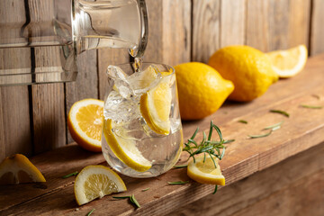 Summer refreshing drink with ice, rosemary and lemon slices on a old wooden table.