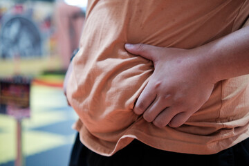 An overweight man holding and pinching the excess fat on his belly.