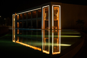 Illuminated modern architecture of luxury hotel reflected in quiet pool at night