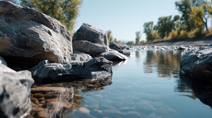 Clear, shallow water flows gently over smooth, dark gray rocks, reflecting the surrounding trees in a serene natural scene.