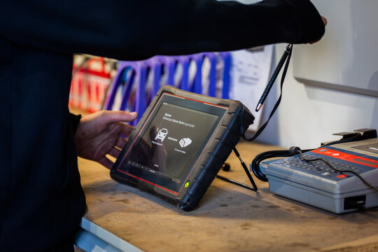 Mechanics hand working on tablet screen used for diagnostics standing on workbench