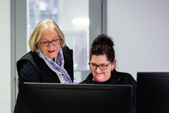 Two female office workers looking at a desktop computer at work together