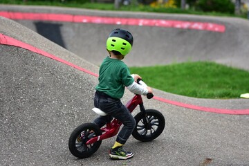 Obraz premium Toddler boy wearing helmet rides red balance bike on asphalt pump track. Active child learning balance and coordination while enjoying outdoor play in park.