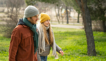 Happy couple wearing winter clothes enjoying a walk in a park on a sunny day