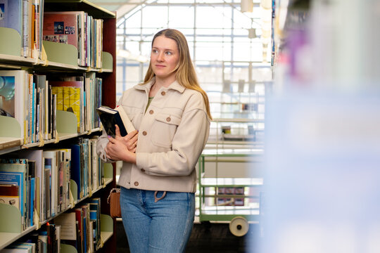 Young woman holding book in uni library with bookshelves