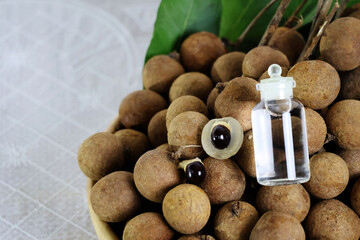 Small glass bottles filled with clear water are placed on several longan fruits, with the peeled fruits having juicy flesh and seeds next to them on a white background.

