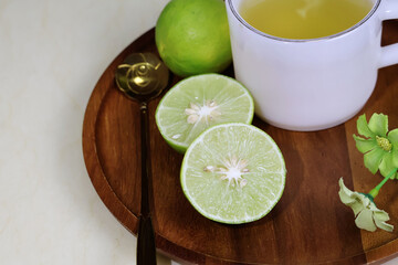 A halved lemon sits next to a white glass of juice on a wooden tray on a cream-colored table.

