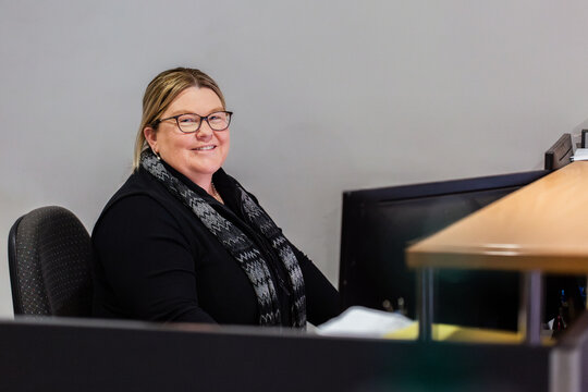 Female office staff seated behind reception desk in front computer