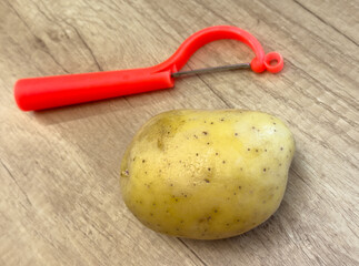Potato with red vegetable peeler on wooden table, kitchen utensil and raw potato prepared for...