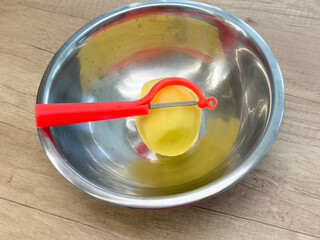 Potato being peeled with red peeler on wooden table, showing vegetable skin removal and kitchen preparation process.