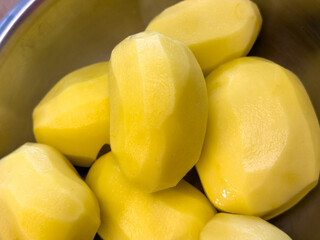 Close-up of peeled potatoes in metal bowl, fresh yellow vegetables prepared for cooking.

