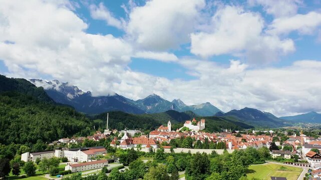 Das Foto zeigt die charmante Altstadt von F&uuml;ssen mit ihren roten D&auml;chern, liebevoll restaurierten Fassaden und dem markanten Turm der Kirche St. Mang. Im Hintergrund erhebt sich das beeindruckende Alp