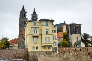 Naklejka premium Yellow building at Schleinufer with Magdeburg Cathedral in the background under a gray overcast sky.