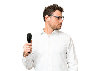 Brazilian man picking up a microphone over isolated chroma key background looking to the side