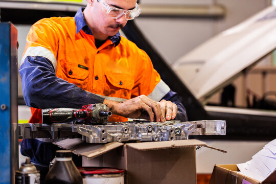 Aussie mechanic working on car engine repairs in workshop wearing high vis