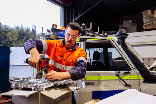 Aussie mechanic working on car engine repairs in workshop wearing high vis