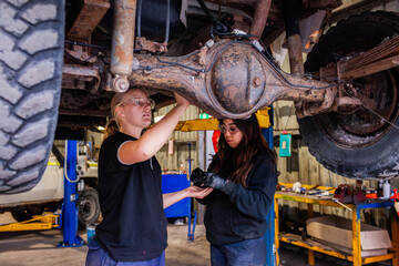 female mechanic tradeswomen working together on car repair in industrial workshop