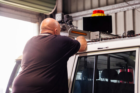 man fitting and installing light bar onto vehicle in mechanics workshop while standing on ladder