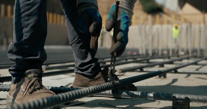 Construction worker weaving and tying steel reinforcement bars at an active building site.