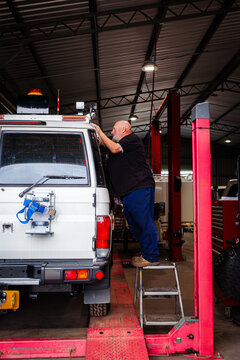 man fitting and installing light bar onto vehicle in mechanics workshop while standing on ladder