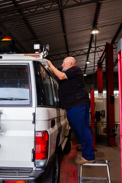 man fitting and installing light bar onto vehicle in mechanics workshop while standing on ladder