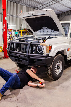 man lying under car installing bull bar onto vehicle in mechanic workshop