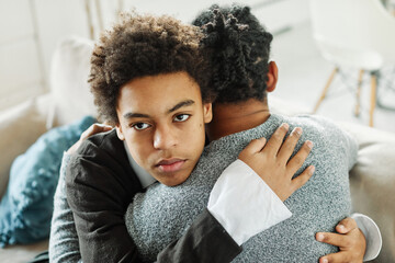 Portrait of son hugging his father, together at home. Son caring for his father, putting hand on his shoulder, comforting and consoling him. Family love, bonding, care and confidence