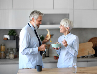 Portrait of a mid aged mature woman and man  couple gettyng ready for work eating breakfast oatmeal...