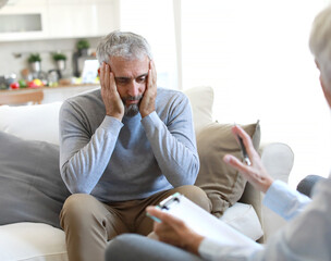 Portrait of a senior mature or mid aged man looking thoughtful or stressed and sad while sitting in session with his female therapist