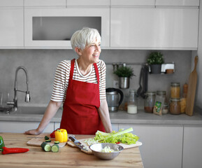 Portrait of happy senior mid aged mature woman prepering meal with fresh vegatebles in kitchen at...