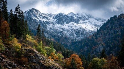 Stunning mountain landscape with vibrant autumn trees meeting snow-capped peaks under a dramatic cloudy sky